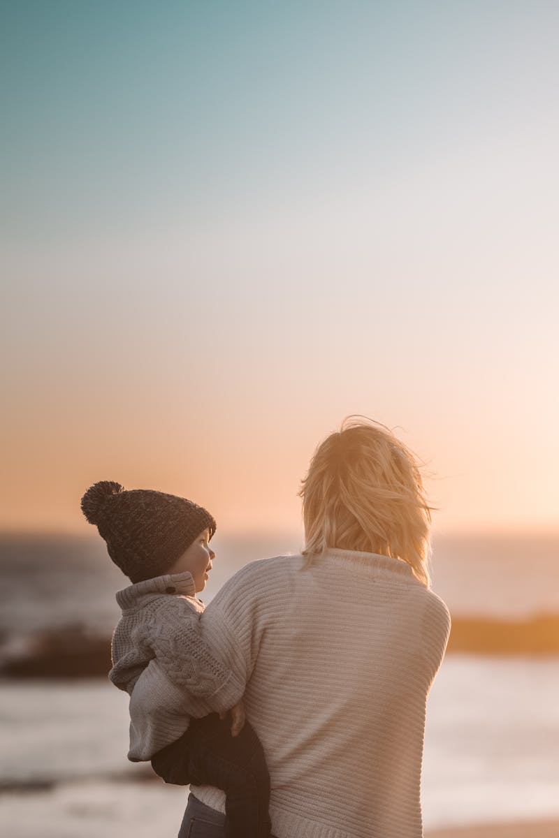 A mother and child share a tender moment on the beach during sunset.